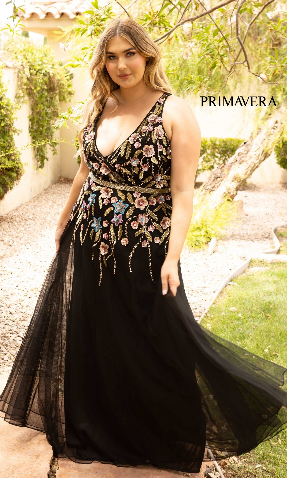 A woman stands outdoors on a stone path near greenery, wearing the Floral-Beaded Long Black Plus-Size Prom Dress. The word